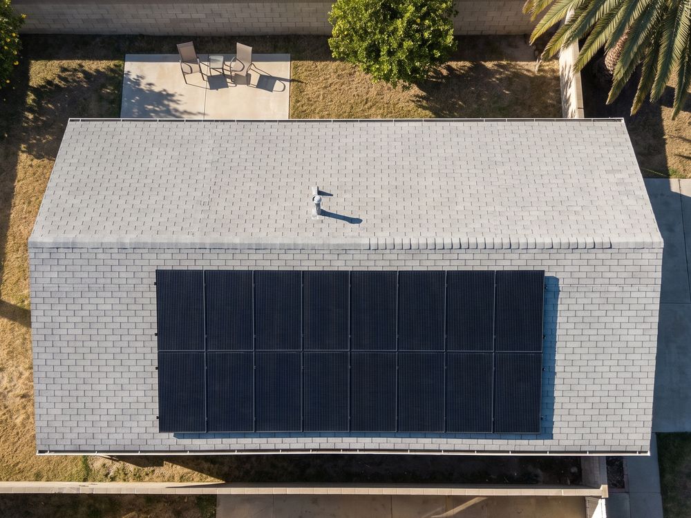 Looking straight down on a single-story ranch house in the San Fernando Valley: two rows of all-black solar panels on a gray shingle roof, with a back patio, a lemon tree and a palm.